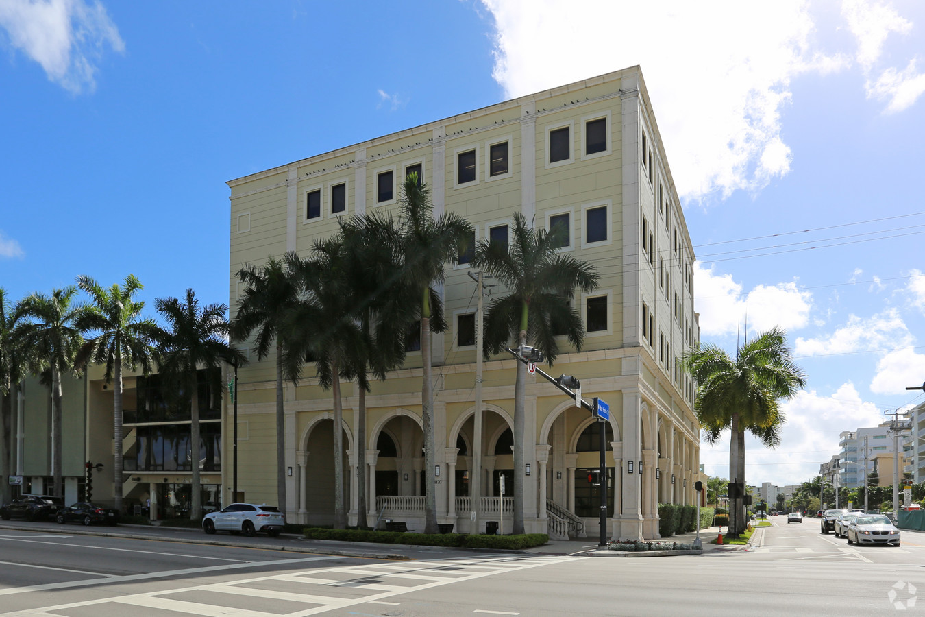 Spanish style office building with arches and palm trees located at an intersection.