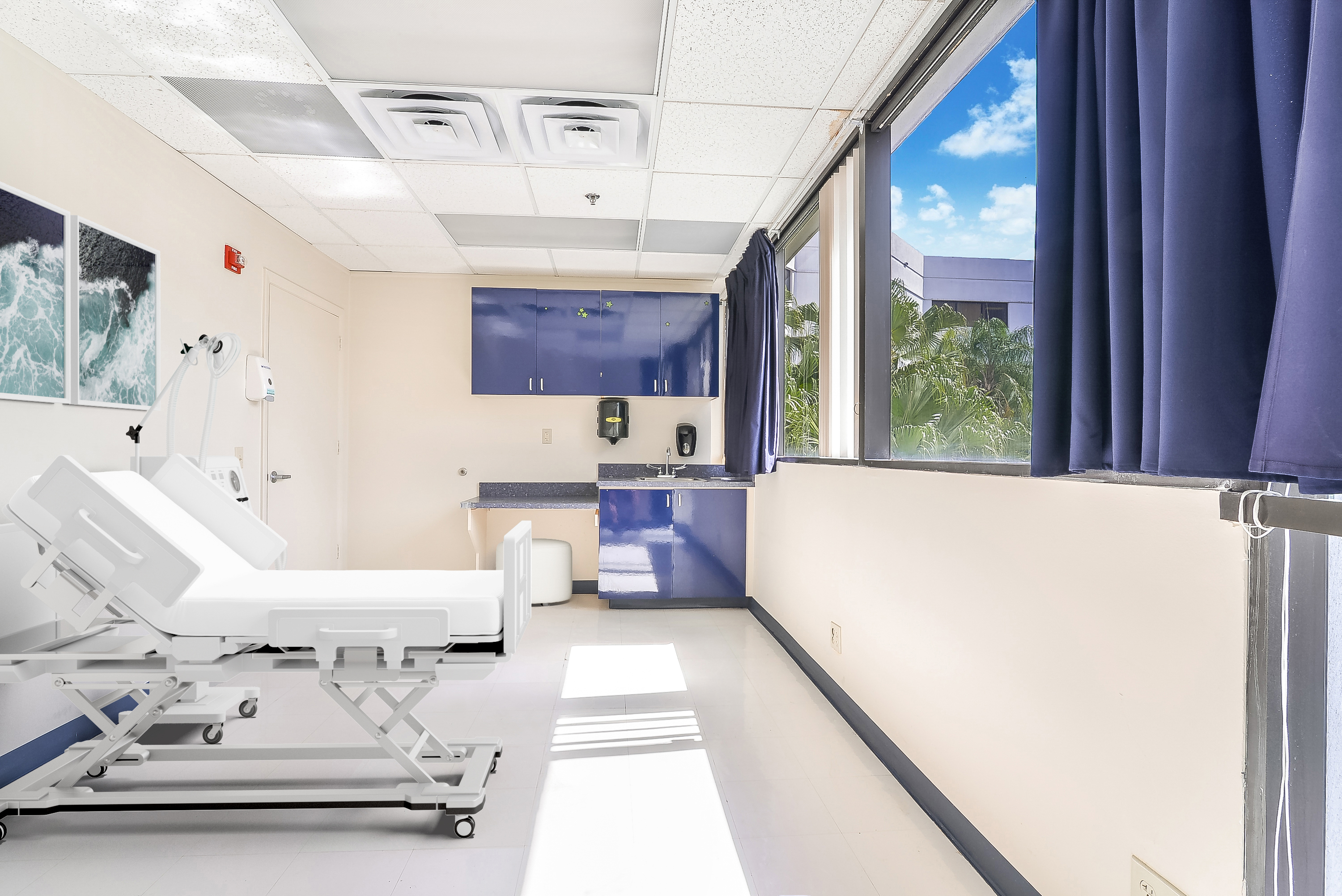 Medical suite with large windows, blue cabinets and patient bed.